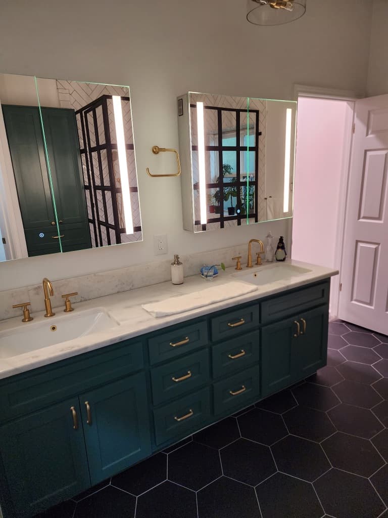 Bathroom remodel in San Antonio TX by Raging Bull Contracting — emerald-green double vanity with brushed-gold faucets and Carrara marble counter on black hex tile floor