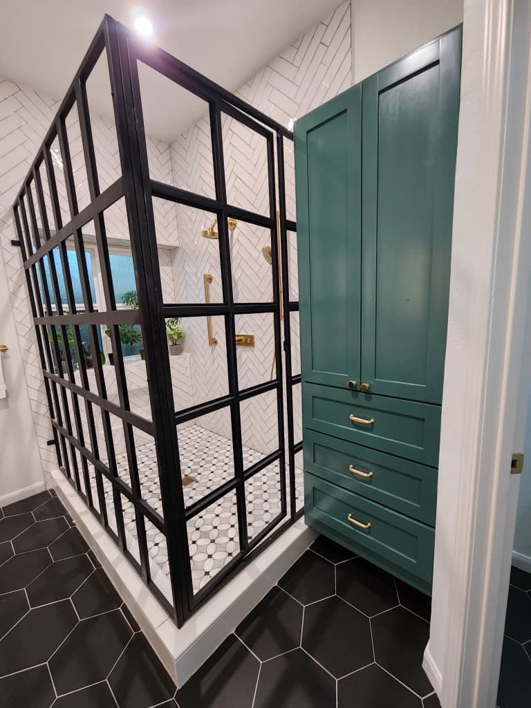 Bathroom remodel in San Antonio TX by Raging Bull Contracting — black industrial-framed glass shower with white herringbone tile and emerald built-in linen cabinet