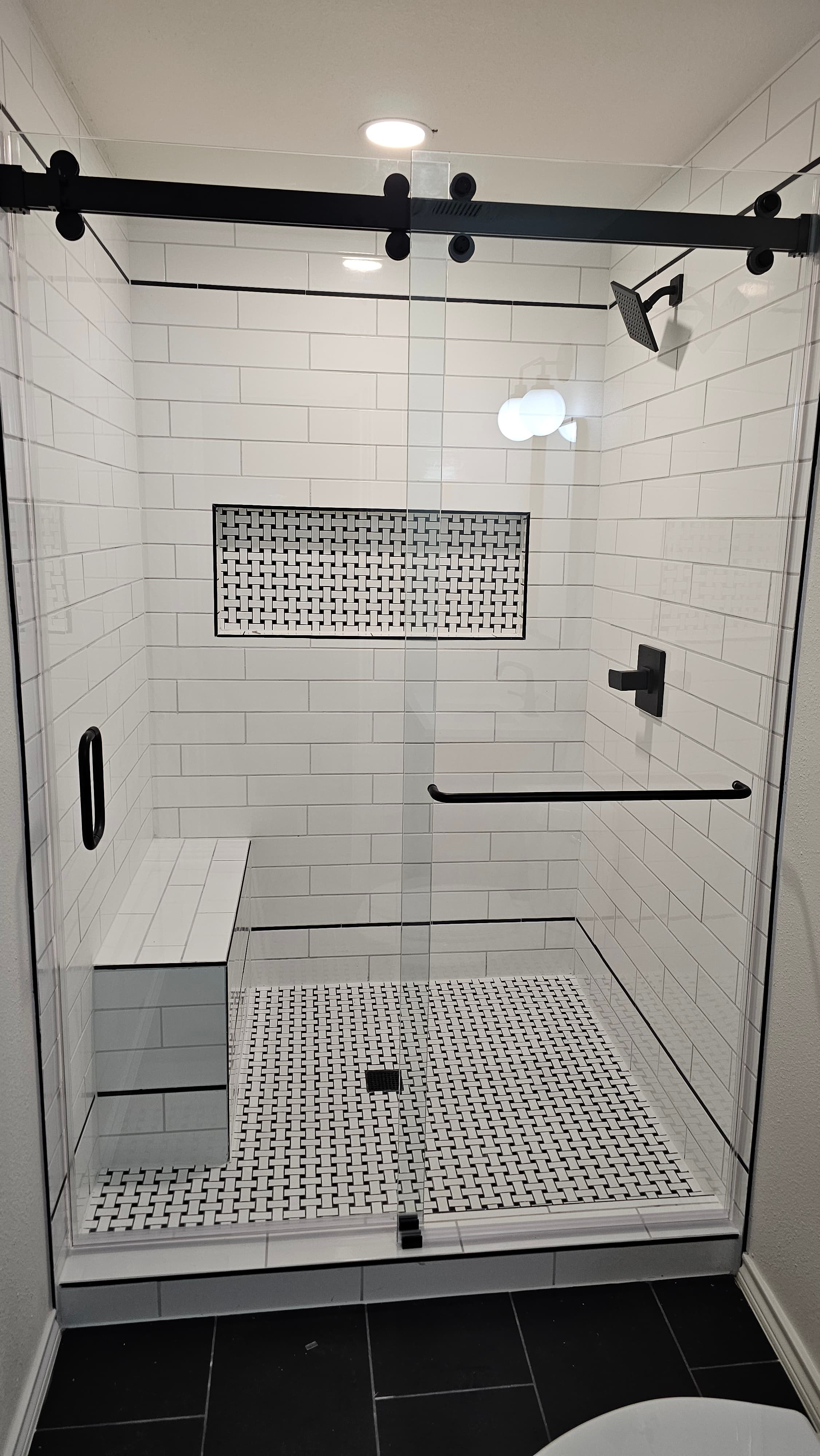 Bathroom remodel in San Antonio TX by Raging Bull Contracting — black-framed glass walk-in shower with vertical white subway tile, basketweave accent niche, and matching basketweave bench