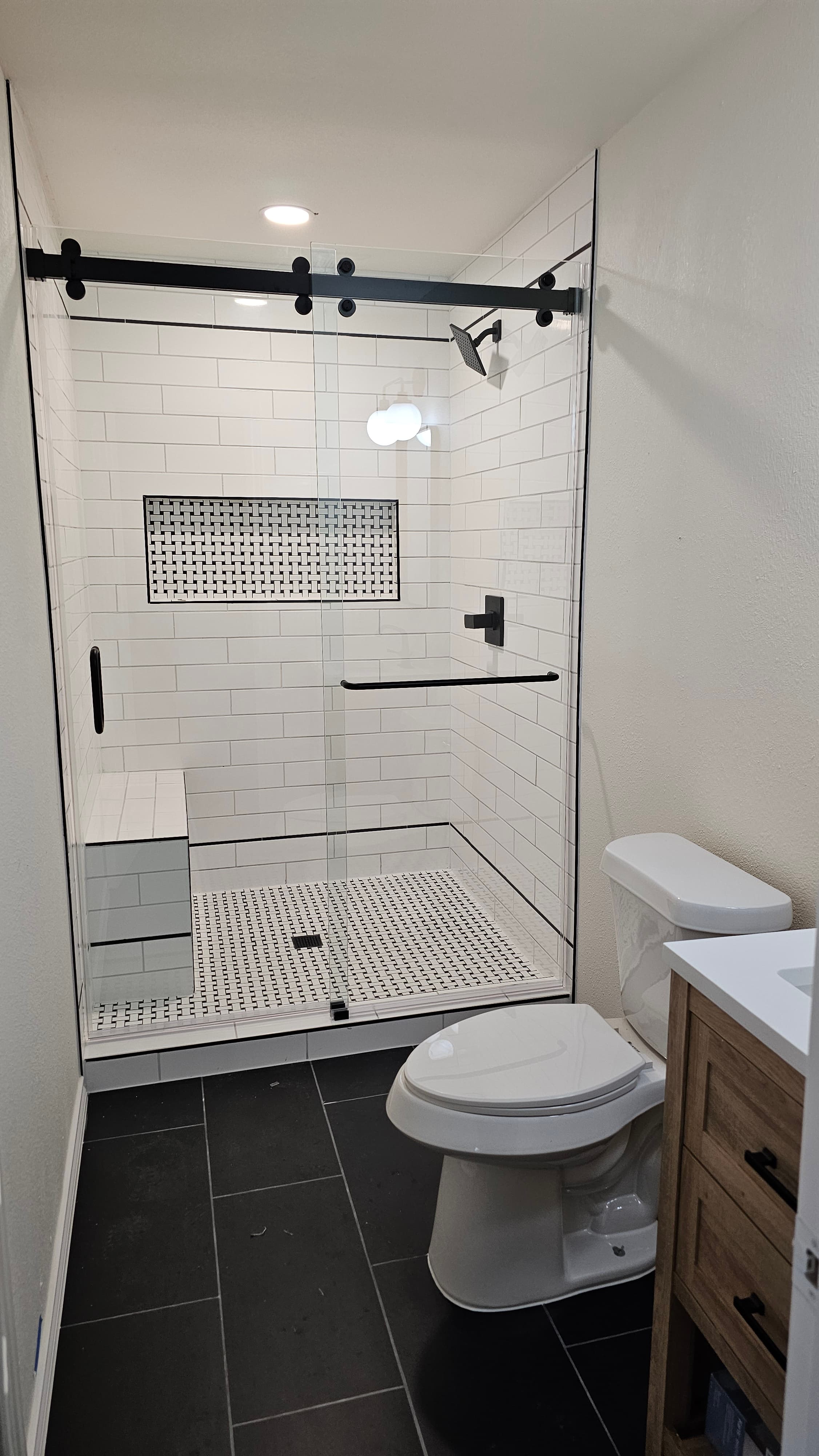 Bathroom remodel in San Antonio TX by Raging Bull Contracting — alternate view of white subway walk-in shower with basketweave bench and dark tile floor