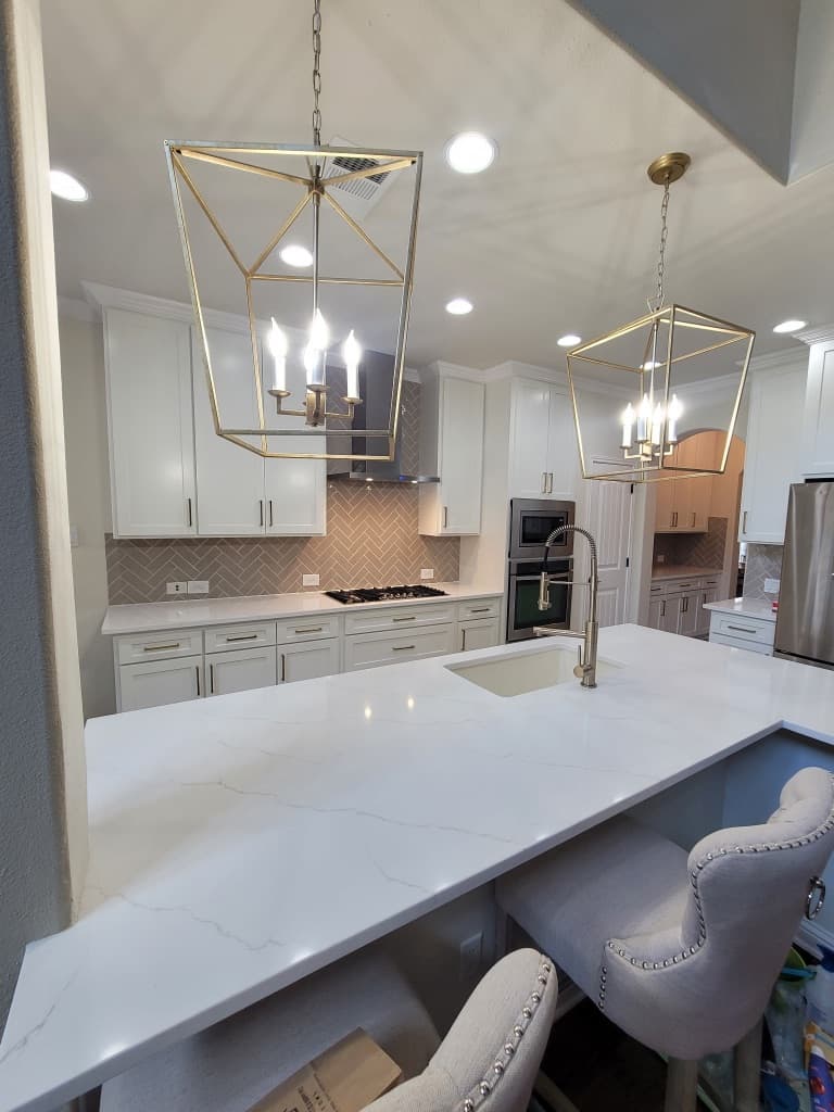 Kitchen remodel in San Antonio TX by Raging Bull Contracting — white Shaker kitchen with brass cage pendant lights, gray herringbone backsplash and waterfall quartz island