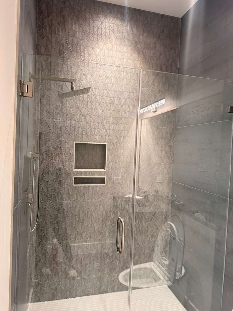 Walk-in shower in Alamo Ranch San Antonio TX by Raging Bull Contracting — sculpted geometric tile feature wall, frameless glass, rain head and handshower with double niche